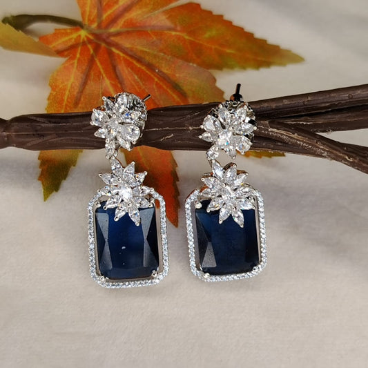 Pair of Diamond Look-alike Earrings with Blue Sapphire Crystal on a White Surface on a  Branch 