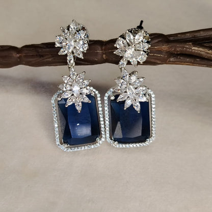 Pair of Diamond Replica Earrings with Blue Genstone on a White Surface hung on Branch