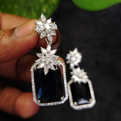 Diamond Replica Earrings with bluestones held by a hand against a dark background