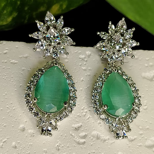 Pair of earrings with green teardrop stones and starburst designs on a textured surface.