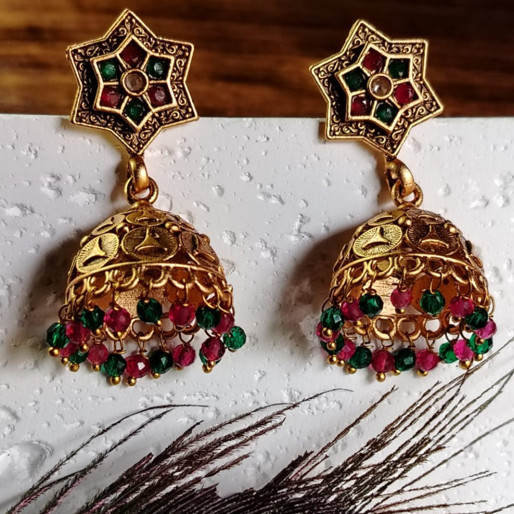 Golden Jhumka Earrings with red and green gemstones on a white surface with a peacock feather