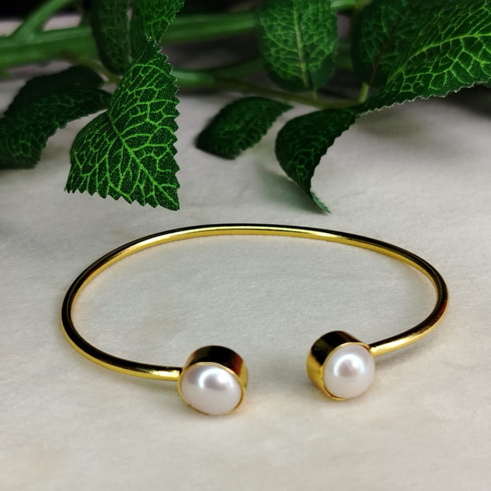 Golden bracelet with pearls on a light surface, with green leaves in the background