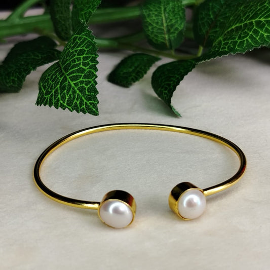 Golden bracelet with pearls on a light surface, with green leaves in the background