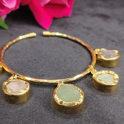 Golden bracelet with gemstone charms on a dark surface with pink flowers in the background