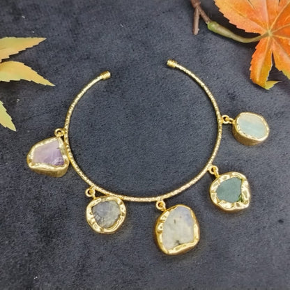 Golden bracelet with natural stone charms on a dark surface with leaves.