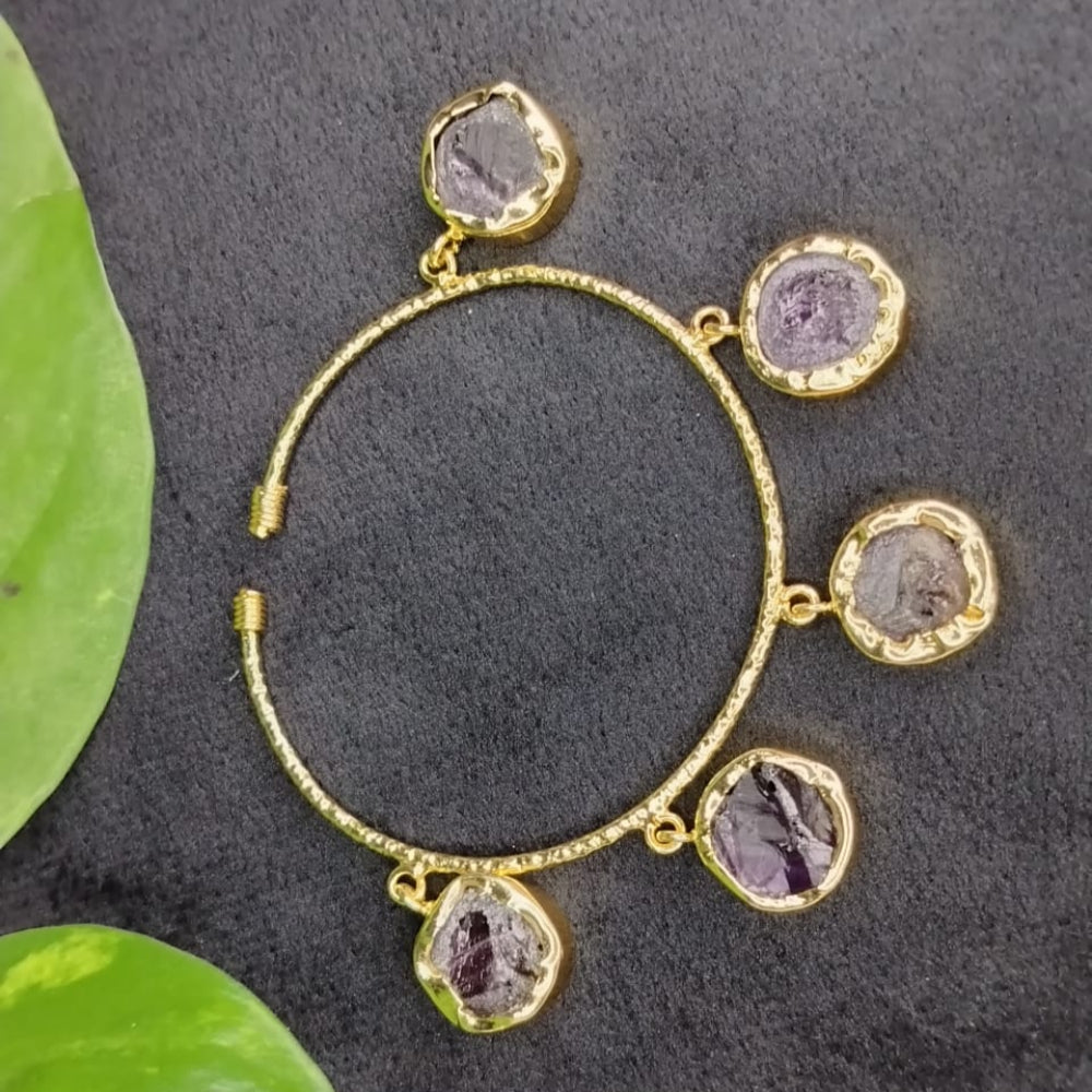 Golden bracelet with Amethyst on a dark surface with green leaves.