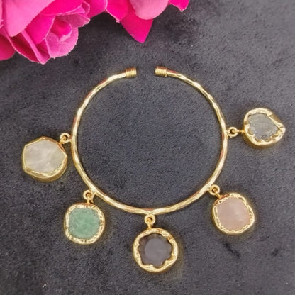 Golden Bracelet with gemstone charms on a dark surface with pink flowers.