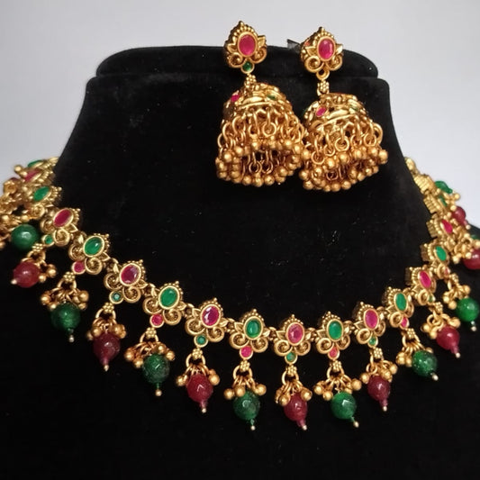 Golden necklace and Jumka Earrings with green and red stones on a black stand