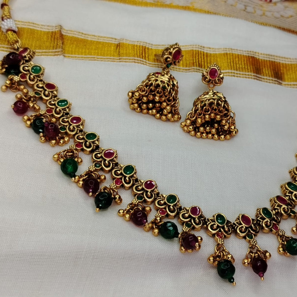 Golden necklace and earrings with green and red stones on a white fabric background