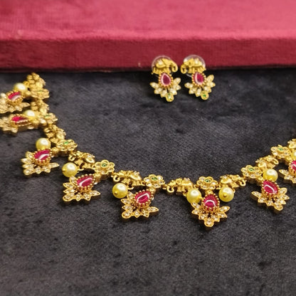 Gold necklace with red gemstones and matching earrings on a dark surface.