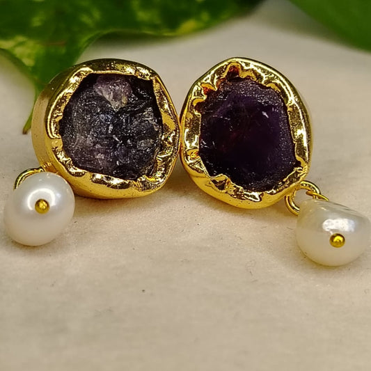 Golden earrings with amethyst gemstones and pearl drops on a beige surface.