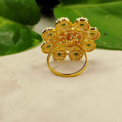 Gold ring with floral design on a beige surface with green leaves in the background