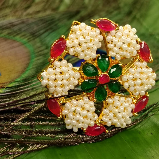 Decorative ring with pearls, red and green stones on a peacock feather background