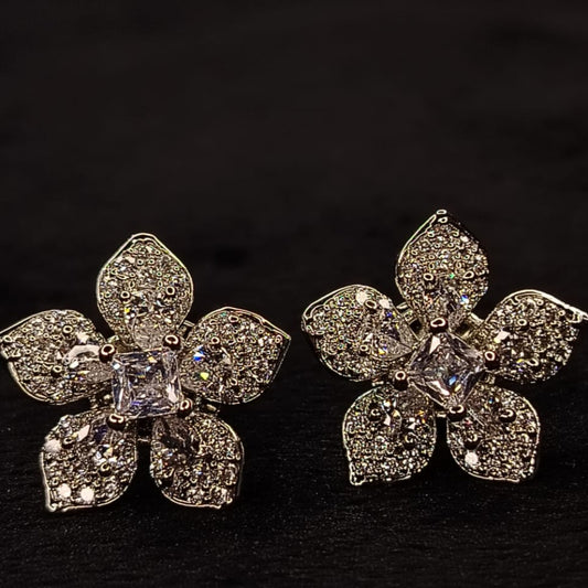 Flower-shaped silver earrings with clear gemstones on a black background