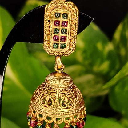 Gold jhumka earring with gemstones on a green leaf background