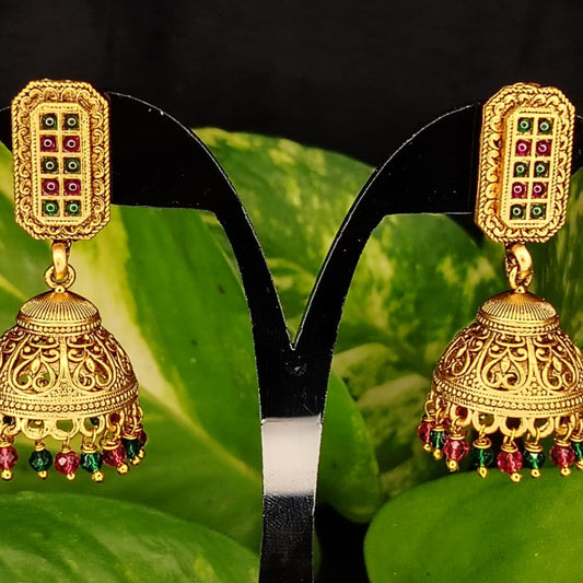 Golden Jhumka with red and green beads on a black stand against a green leaf background