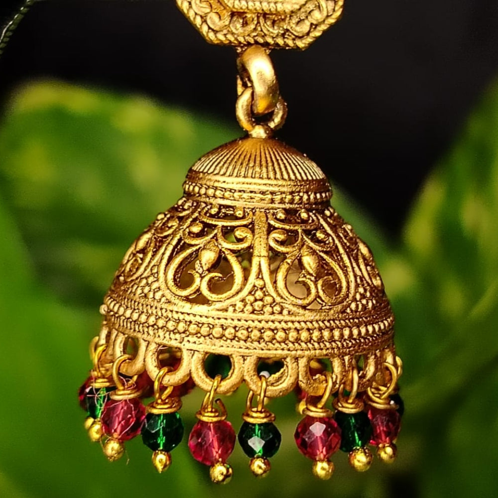 Golden jhumka earring with red and green gemstones on a leaf background