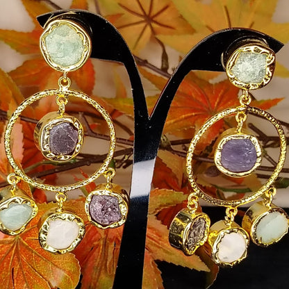 Golden earrings with colorful natural stones on a stand with autumn leaves in the background