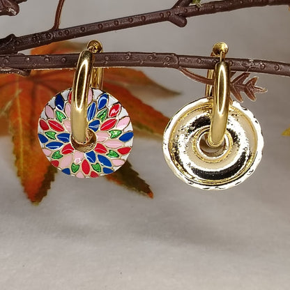 Gold earrings with colorful circular design on a branch with leaves