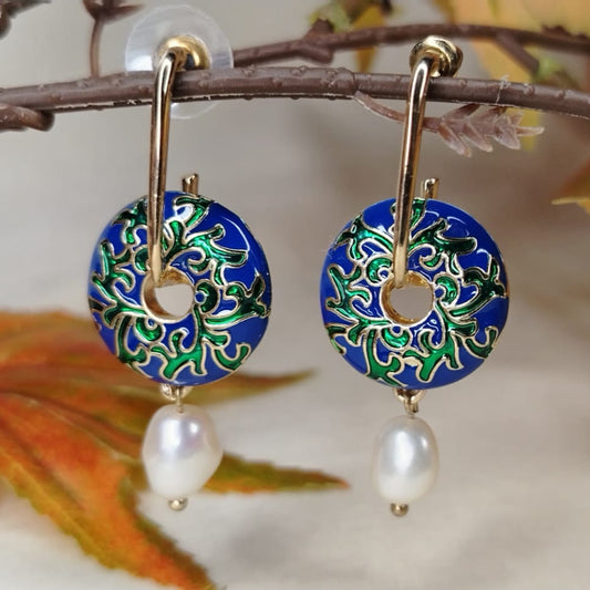 Pair of earrings with blue circular designs and pearl-like beads on a branch with leaves.