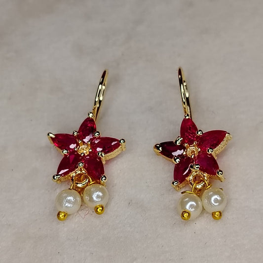 Pair of earrings with red flower-like designs and pearl beads on a light background
