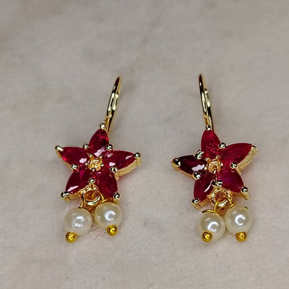 Pair of earrings with red crystal flower-like designs and pearl beads on a light background