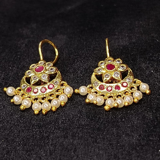 Pair of golden ear cuffs with pearl beads and red stones on a black background