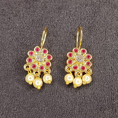Pair of gold earrings with pearls and red stones on a gray background