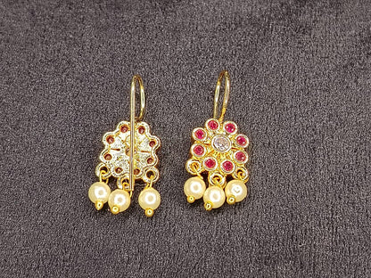 Gold earrings with pearls and red stones on a gray background