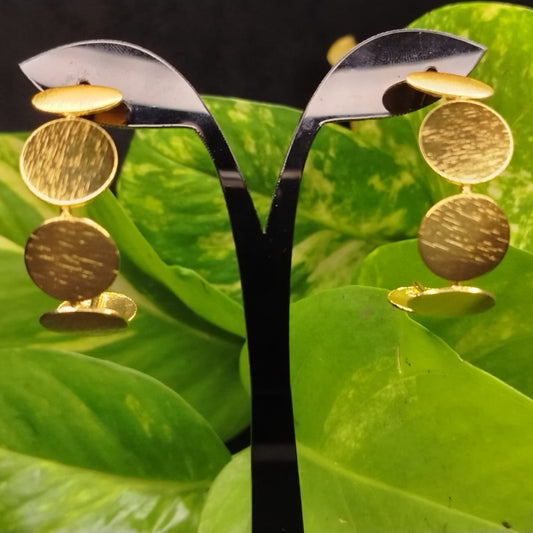 Golden earrings on a stand with green leaves in the background
