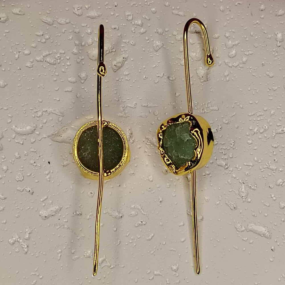 Gold earrings with green stone on a textured white surface