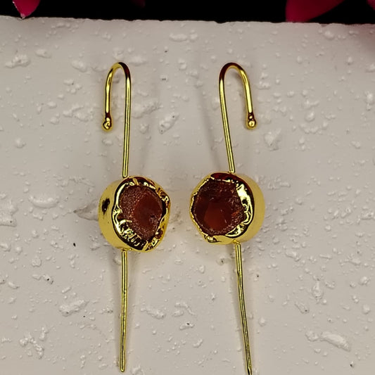 Gold earrings with red gemstones on a textured white surface.