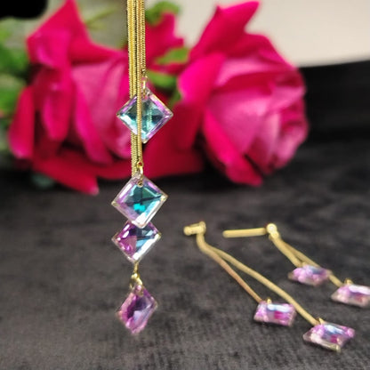 Gold earrings withrainbow crystal gemstones in front of pink flowers