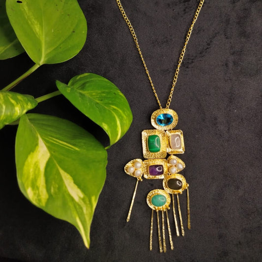 Gold necklace with gemstone pendant on a dark background with green leaves.
