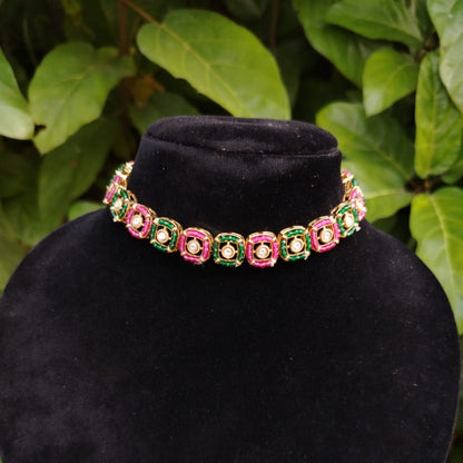 Necklace with pink and green stones on a black velvet stand against a leafy green background