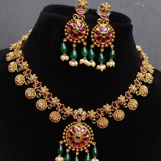 Gold necklace with green beads and red stones on a black stand