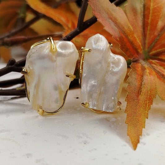 Pair of pearl earrings with gold accents on a white surface with autumn leaves in the background
