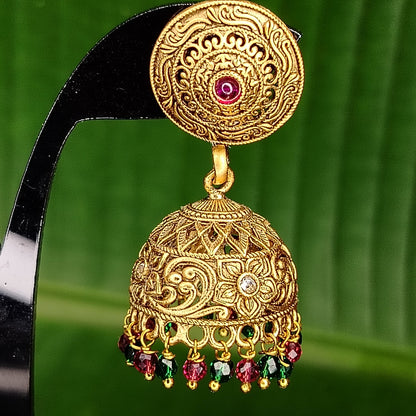 Golden  jhumka earring with red and green stones on a green leaf background