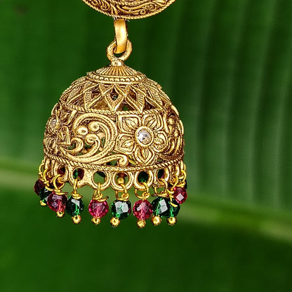 Golden jhumka with gemstones on a green background