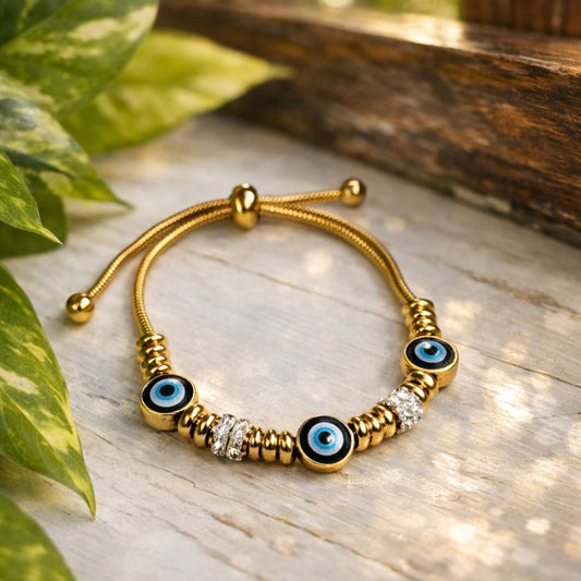 Golden  bracelet with blue eye beads on a wooden surface with leaves in the background